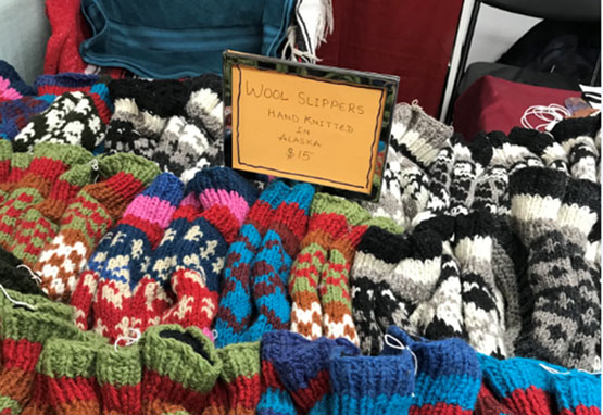 Colorful wool slippers with a sign reading Woll Slippers Hand Knitted in Alaska $15